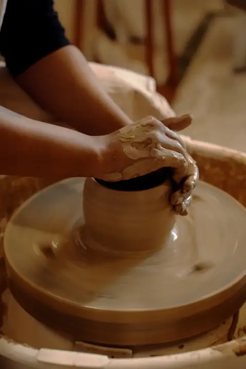 Clay-covered hands pulling the wall of a pot on a spinning wheel
