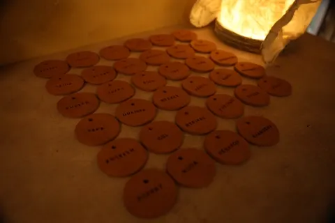 Hand-stamped clay name tags drying under a paper lamp