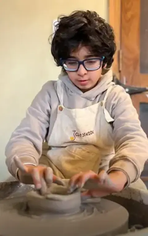 A young maker centering clay on the pottery wheel