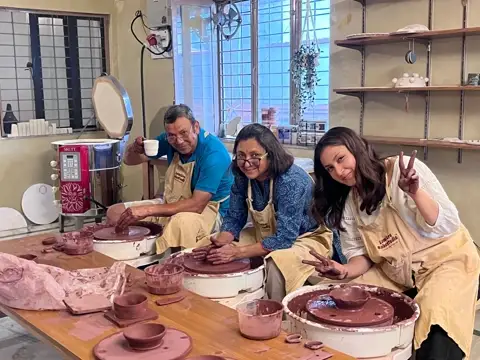 A family of three at the wheels in the studio, aprons on, mid-session