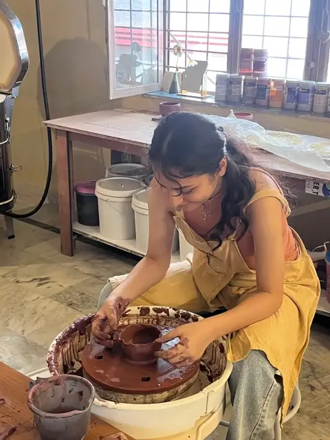 A maker throwing a wide bowl at the wheel beside the kiln