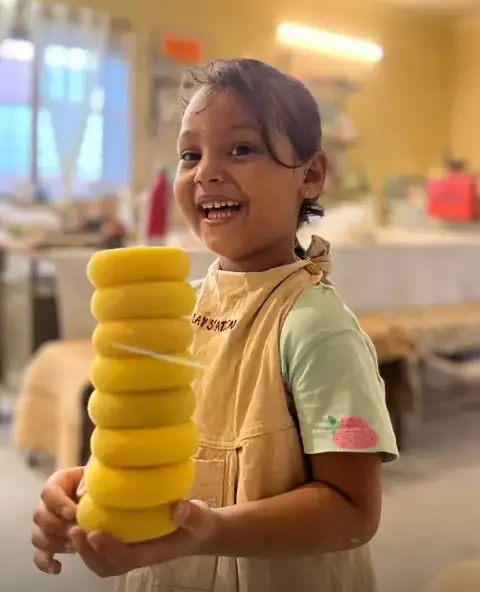 A young maker beaming with a tower of yellow sponges