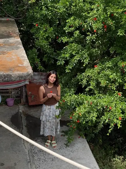 Harshita in the garden at The Nook, holding a pomegranate flower