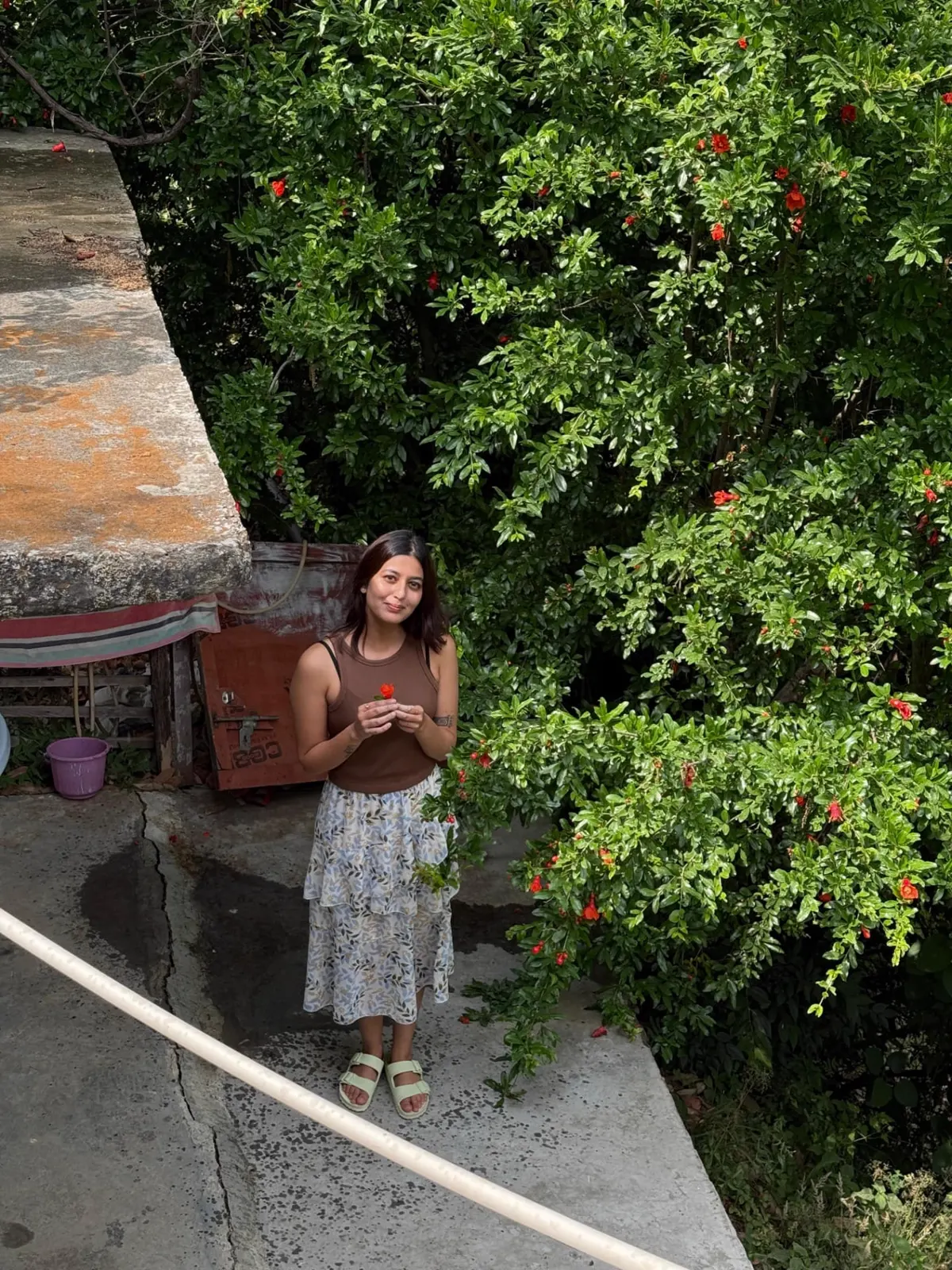 Harshita in the garden at The Nook, holding a pomegranate flower