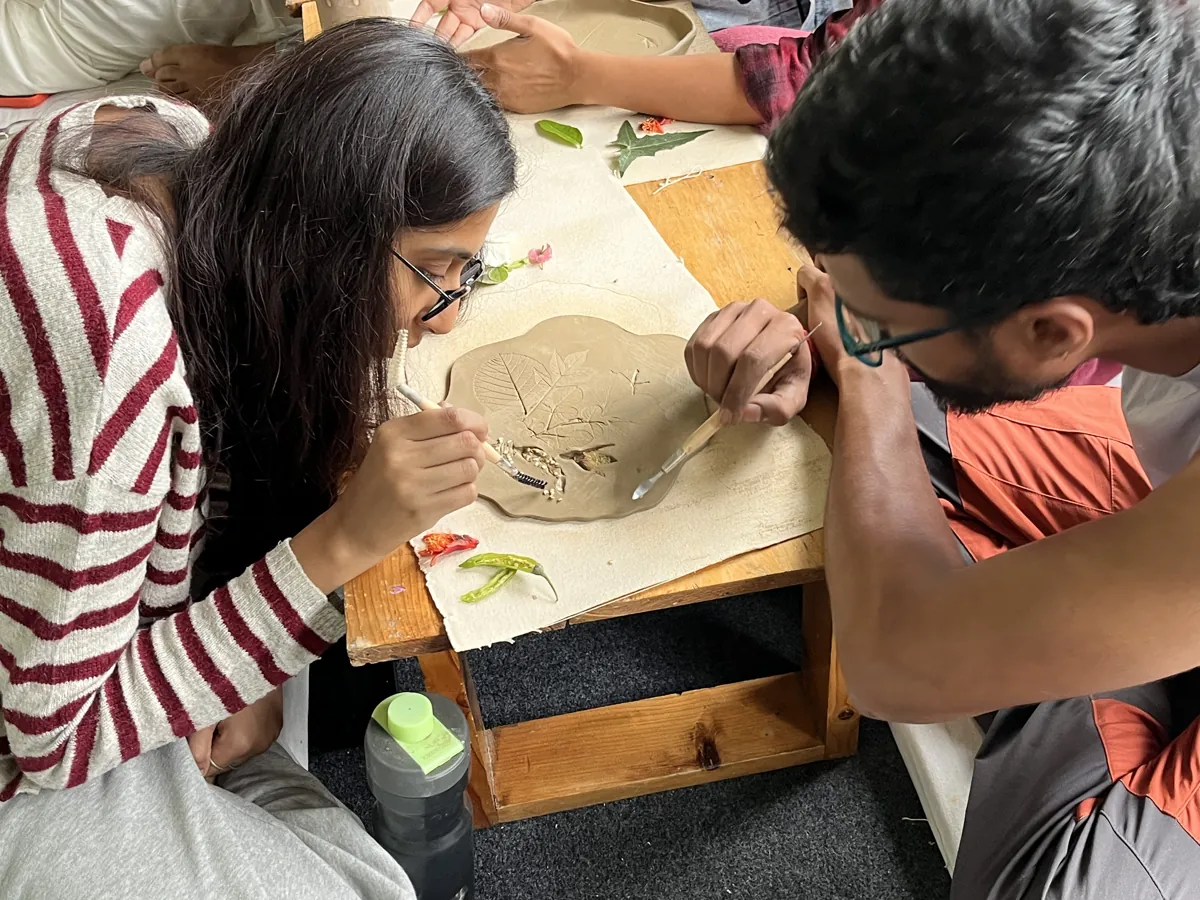 Two guests carving a slab of clay together at the work table