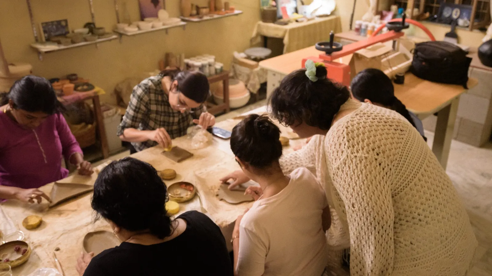 Hands working slabs of clay across a canvas-covered table