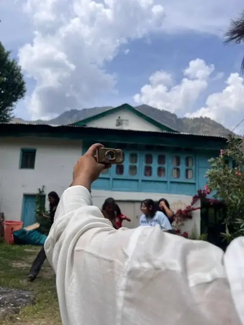 A clay camera held up in front of the blue mountain house
