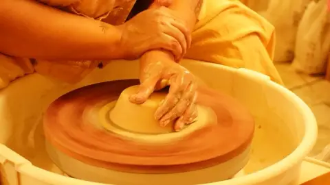 Clay-covered hands centering a mound of clay on the wheel in warm light