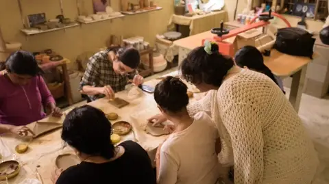 Hands working slabs of clay across a canvas-covered table