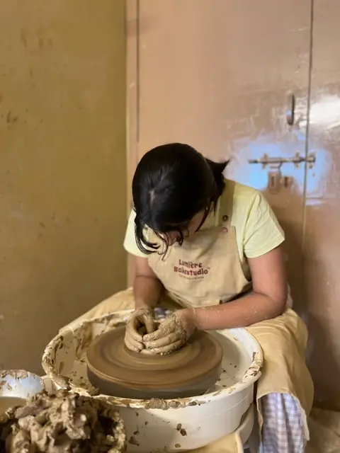 A guest centring clay on the wheel in a Lumière apron