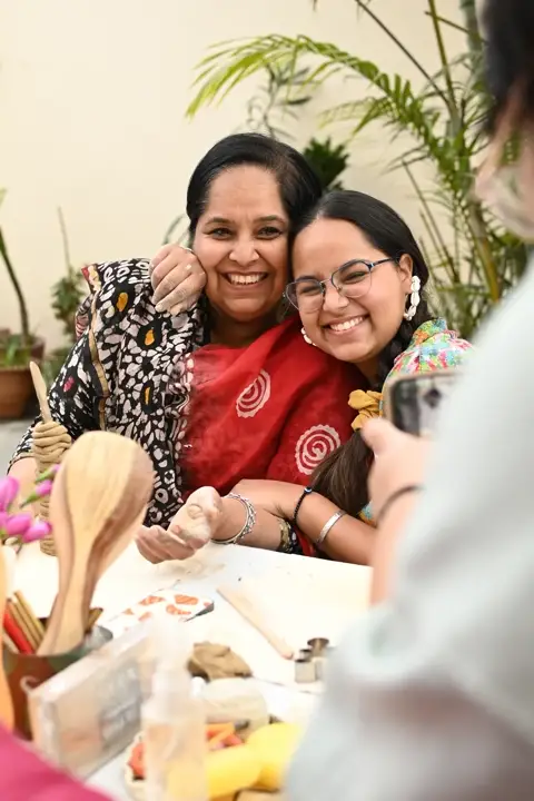 Two makers laughing, cheek to cheek, at the hand-building table