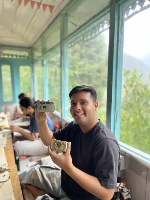 A guest holding up his finished clay camera in the sunroom