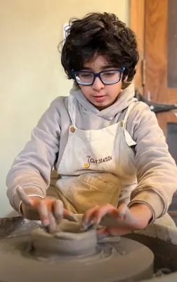 A young maker centering clay on the pottery wheel
